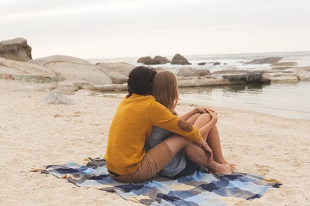 Side view of Caucasian couple relaxing together sitting at beachの写真素材