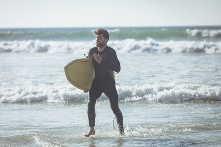 Front view of young Caucasian male surfer with a surfboard running out of the water on a beach. He is holding his surfboardの写真素材