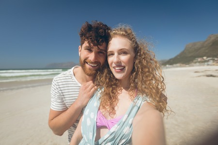 Portrait of romantic Caucasian couple standing at beach on a sunny day. The are smiling and looking...