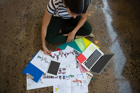 High angle view of smart Hispanic woman sitting on the ground with legs-crossed in front of documents and laptop at creative officeの写真素材