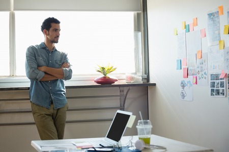 Front view of young mixed race man looking at wall with sticky notes and documents standing in...