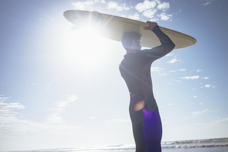 Low angle view of young Caucasian male surfer holding surfboard on his head at beach on sunny dayの写真素材