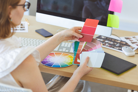 High angle view of young Caucasian graphic designer checks the color with color swatch at desk in office