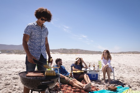 Front view of group of Multi ethnic friends having fun in preparing a barbecue and chilling together at beach in the sunshineの写真素材