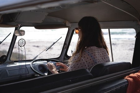 Rear view of beautiful caucasian woman driving camper van at beach on a sunny day