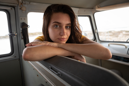 Portrait of beautiful Caucasian woman sitting in camper van and looking at the camera against beach in backgroundの写真素材