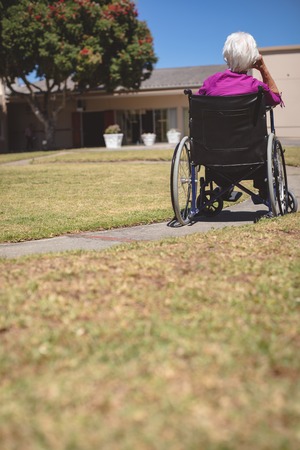 Rear view of senior Caucasian woman relaxing on wheelchair at nursing home parkの写真素材