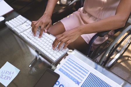 Mid-section of young disabled mixed-race businesswoman working on computer at desk in the officeの写真素材