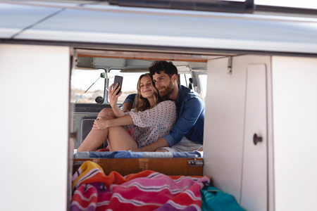 Front view of  caucasian couple taking selfie in camper van at beach on a sunny dayの写真素材