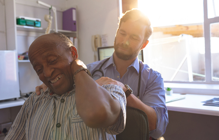 Front view of Caucasian male doctor checking neck of a senior man in clinicの写真素材