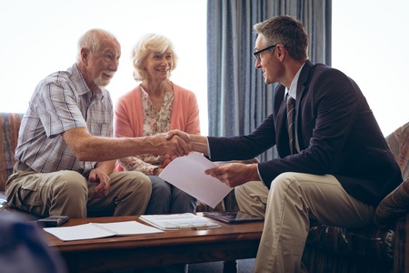 Front view of matured Caucasian male physician interacting with senior Caucasian couple at retirement home. Both men shaking handsの写真素材