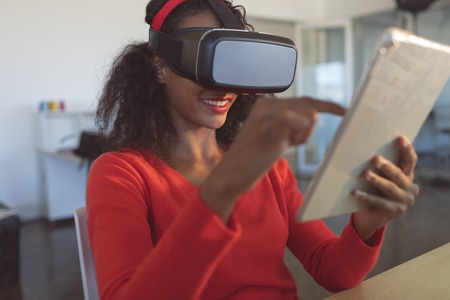 Front view of young mixed-race female graphic designer using multimedia devices at desk in a modern...