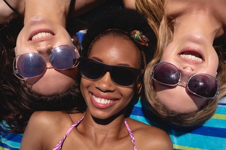 Close-up of happy beautiful young multi ethnic women with sunglasses lying on beach in the sunshine