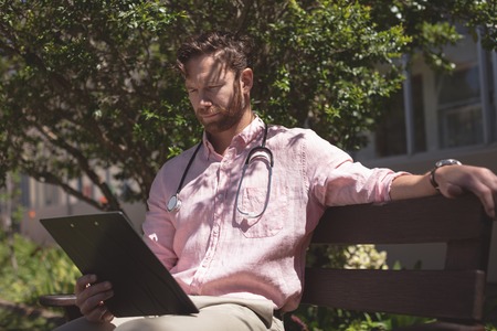 Front view of confident Caucasian male doctor holding medical report while he is sitting on bench...
