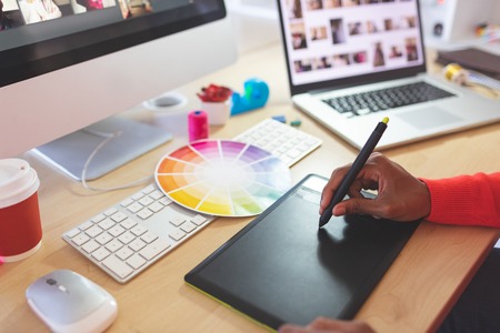 Close-up of young mixed-race female graphic designer using graphic tablet at desk in a modern officeの写真素材