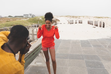 Rear view of handsome African American man capturing photo of beautiful Mixed-race woman while standing at pavement on a sunny dayの写真素材