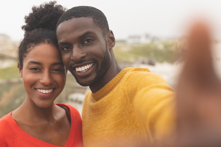 Portrait of romantic Multi-ethnic couple standing near promenade with dune on the background. They are smiling and looking at cameraの写真素材