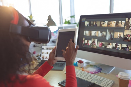 Rear view of young mixed-race female graphic designer using multimedia devices at desk in a modern officeの写真素材