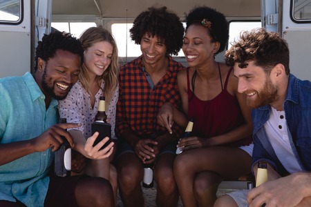 Front view of multi ethnic friends laughing together while they drinking beer bottle on a caper van