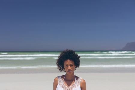 Portrait of beautiful young mixed-race woman looking at camera standing at beach on a sunny dayの写真素材