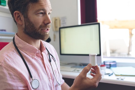 Side view of a Caucasian male doctor prescribing pills to his patient in clinic roomの写真素材