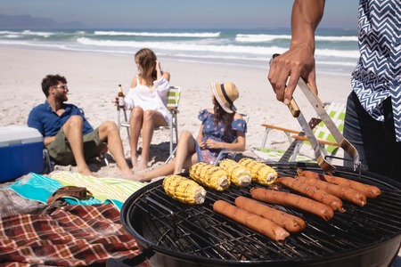 Mid-section of Mixed-race man doing a barbecue while his friends chilling at beach in backgroundの写真素材