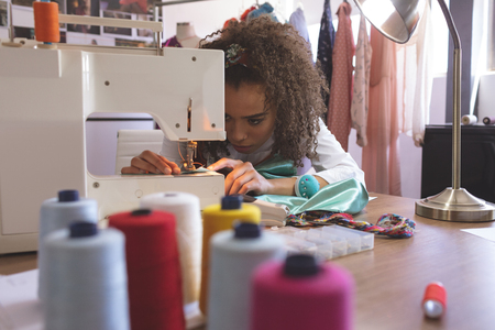 Front view of young Mixed-race female fashion designer working with sewing machineの写真素材