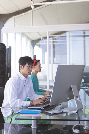 Side view of Multi-ethnic business people working on computer at desk in modern officeの写真素材