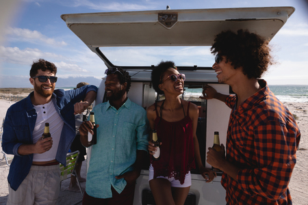 Front view of group of multi-ethnic friends enjoying at beach while standing near camper van against ocean in backgroundの写真素材