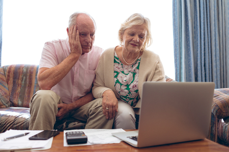 Front view of senior Caucasian couple looking medical report on laptop at retirement homeの写真素材
