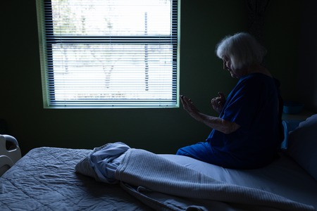 Side view of a senior Caucasian female patient using a mobile phone while sitting on a hospital bedの写真素材