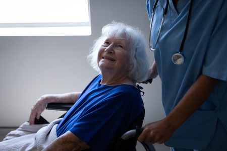 Side view of a Caucasian female surgeon pushing the wheelchair of a disabled senior Caucasian...