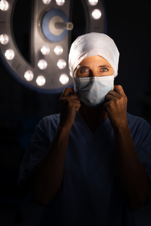 Portrait of a Caucasian female surgeon putting on an operation mask and looking at the camera in the operation room in hospitalの写真素材