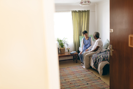 Front view of Asian female doctor and senior African american  male patient interacting with each other at retirement homeの写真素材