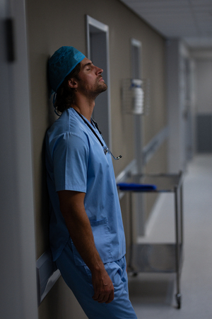 Side view of a Caucasian male surgeon leaning against a wall in the corridor at hospitalの写真素材