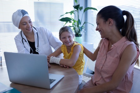 Front view of matured mixed race female doctor and mother talking with Caucasian girl patient in clinic at hospitalの写真素材