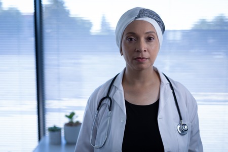 Portrait of matured mixed race female doctor standing  and looking at camera in clinic at hospitalの写真素材