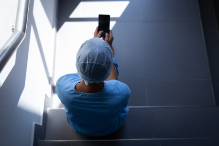 Overhead view of a Caucasian female surgeon using her mobile phone while sitting on hospital stair caseの写真素材