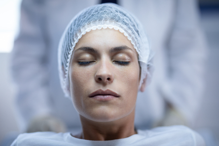 Front view of a Caucasian female patient sitting with eyes closed on bed at hospitalの写真素材