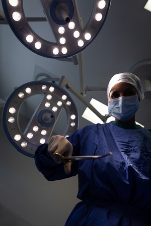 Low angle view of a mature Caucasian female surgeon holding surgical scissor in her hand in clinic