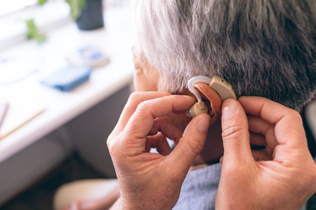 Middle section of Caucasian male doctor applying hearing aid to senior mixed race woman ear in clinic at retirement homeの写真素材