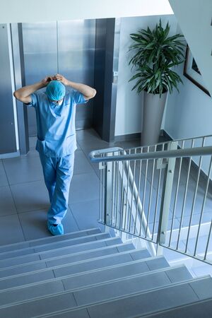 High angle view of Caucasian male surgeon wearing surgical mask while standing at stairsの写真素材