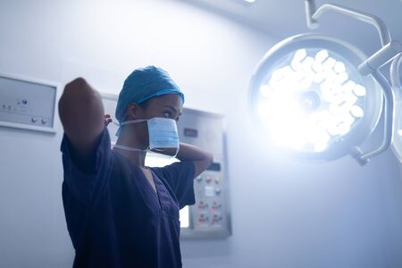 Low angle view of young Mixed-race female surgeon wearing surgical mask in operation theater at hospitalの写真素材
