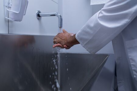 Mid section of Caucasian male surgeon washing hands in sink at hospitalの写真素材