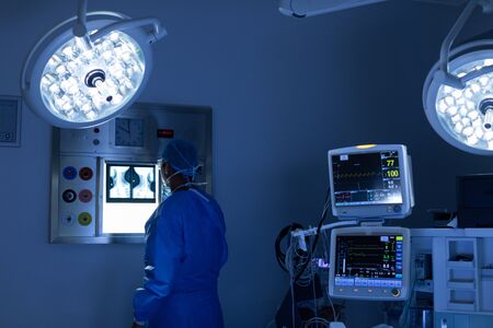 Rear view of Caucasian male surgeon reading x ray in operating room at hospitalの写真素材
