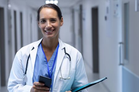 Front view of happy Mixed-race female doctor looking at camera in the corridor at hospital