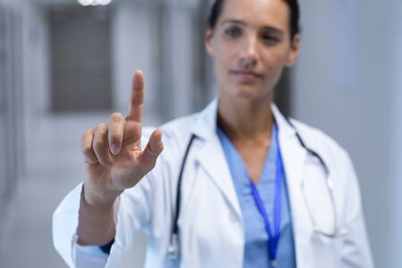 Front view of Mixed-race female doctor pretending to touch an invisible screen in the corridor at hospitalの写真素材