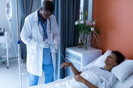 Front view of African-american male doctor injecting injection to female patients intravenous drip in the ward at hospitalの写真素材