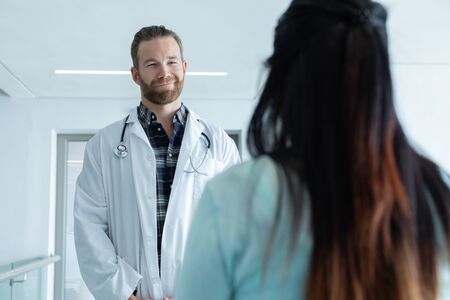 Front view of Caucasian male doctor interacting with pregnant woman in the corridor at hospitalの写真素材