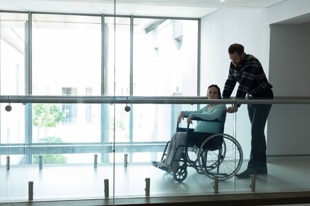 Side view of Caucasian man pushing pregnant woman on wheelchair in the corridor at hospital